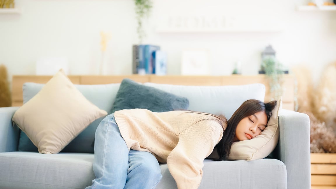 Asian woman resting at home on couch, feeling exhausted after wo